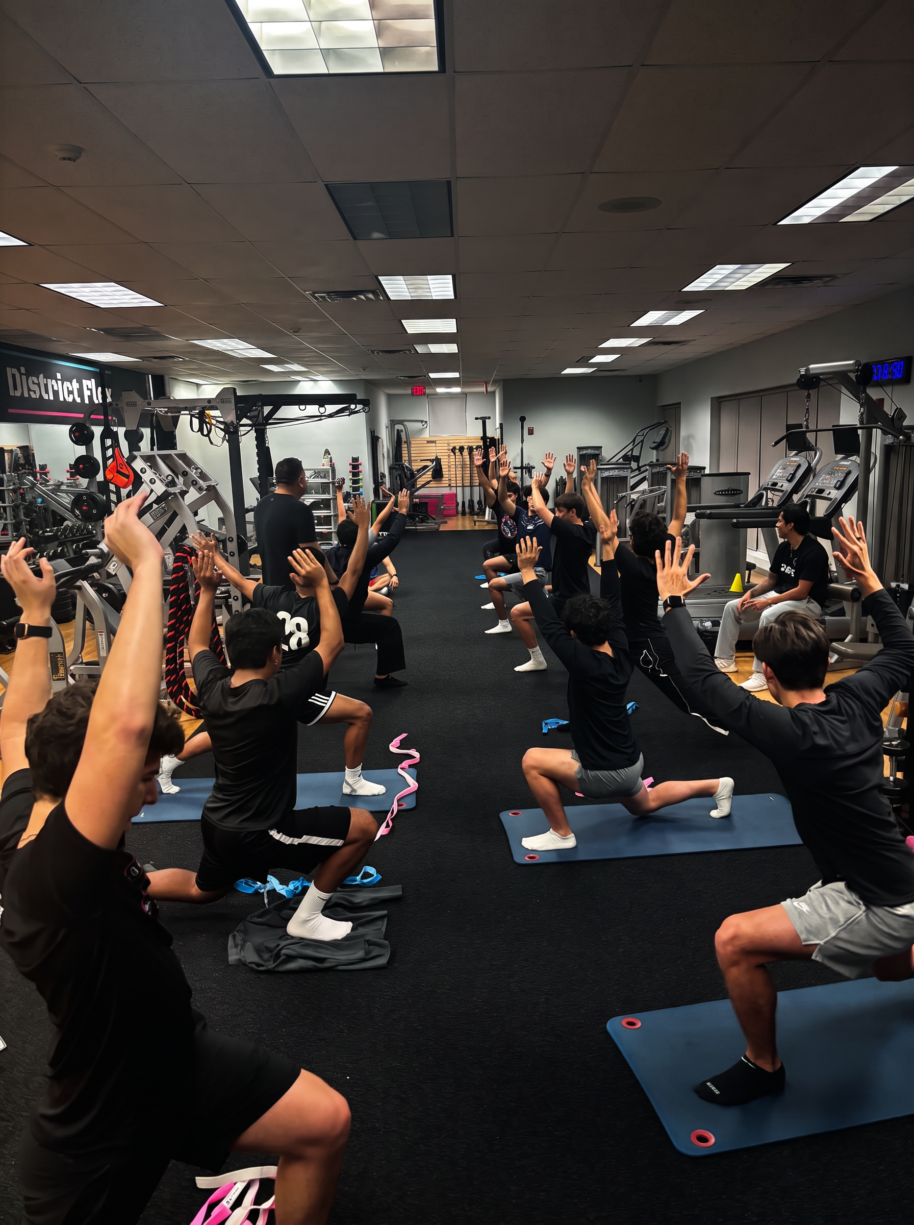 Large group class at District Flex holding a kneeling overhead reach stretch on mats